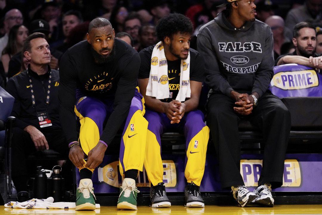 Los Angeles Lakers forward LeBron James, second from left, and guard Bronny  James, second from right sit together during the first half of an NBA  basketball game against the Brooklyn Nets, Friday,